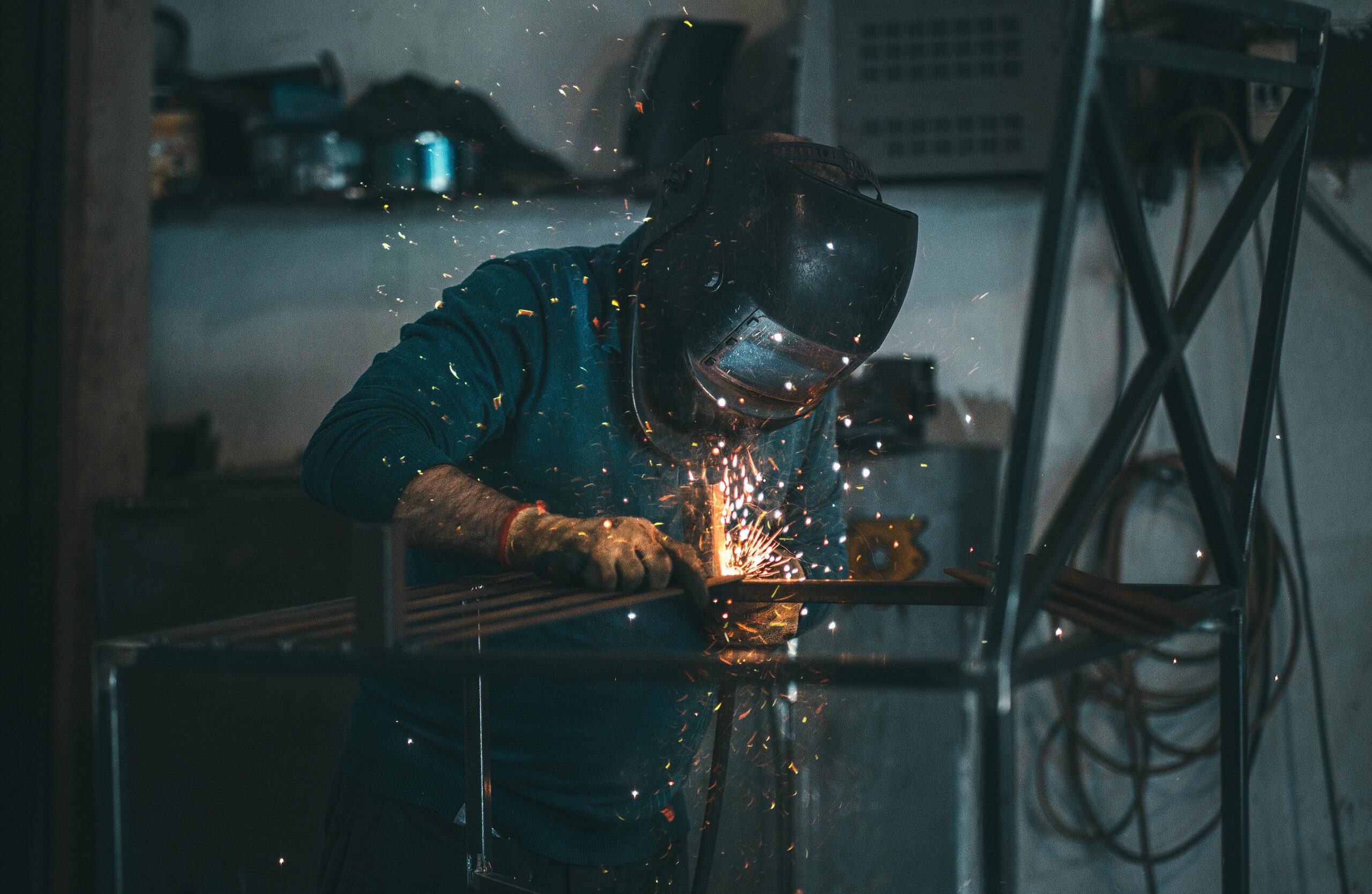 Skilled welder works with sparks in an industrial workshop setting, wearing safety gear.