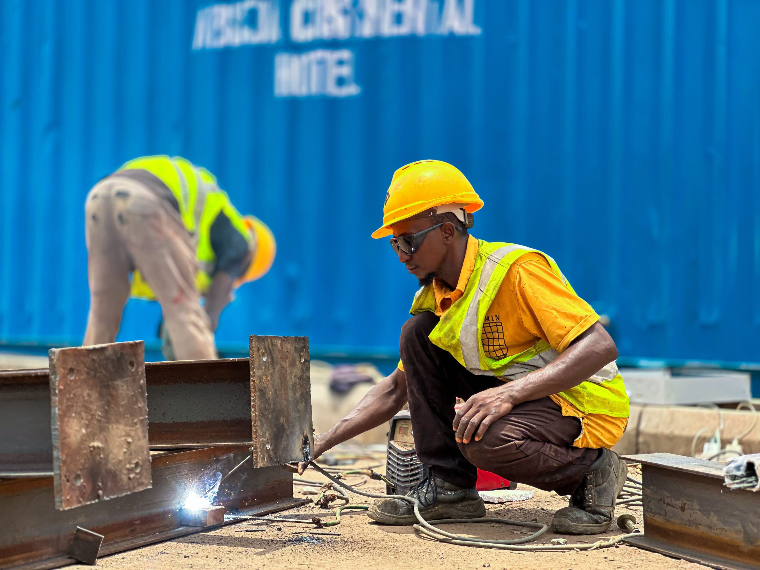A construction worker wearing safety gear welds steel beams at an outdoor site.