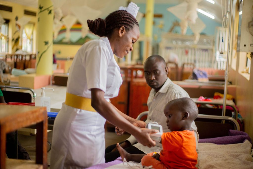 A nurse attends to a young patient while a guardian looks on in a hospital ward.